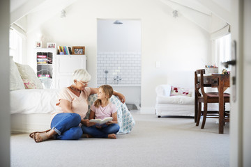 Grandmother and granddaughter reading a book in her bedroom