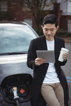 Man using digital tablet while charging car