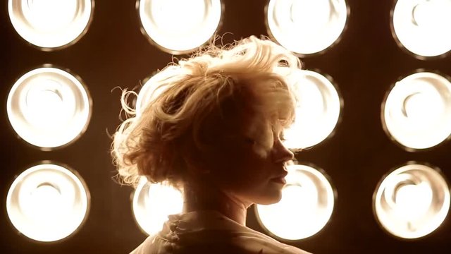 Young female blonde caucasian dancer dancing in front of studio light. Closeup shot.