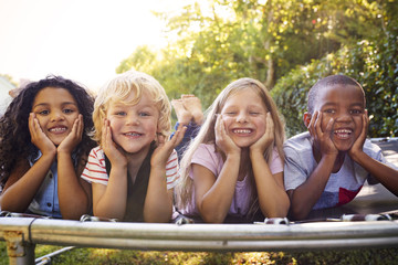 Four kids lying down together on a trampoline in the garden