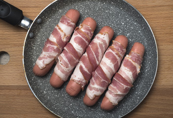 Preparation of raw sausages wrapped spirally in bacon on a frying pan.