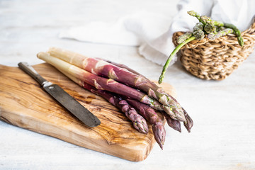 purple asparagus on wooden cutting board with knife
