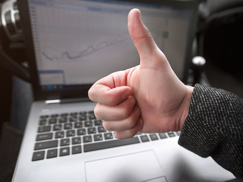 Man shows thumbs up on laptop background with graph of sales growth.  Remote job. Man working while being in the car. .
