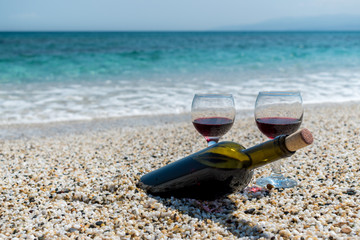 Glasses of red wine and bottle on the beach at the summer sunny day. Sea on the background.