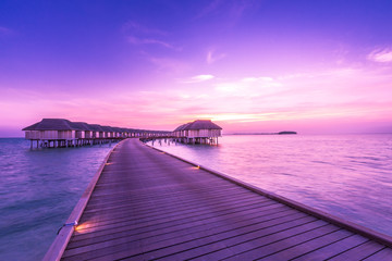 Sunset on Maldives island, luxury water villas resort and wooden pier. Beautiful sky and clouds and...
