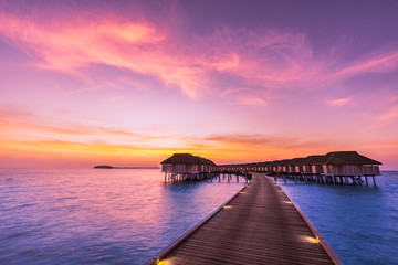 Sunset on Maldives island, luxury water villas resort and wooden pier. Beautiful sky and clouds and beach background for summer vacation holiday and travel concept