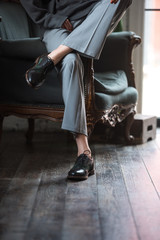 low section of girl in leather shoes and stylish pants sitting on armchair