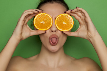 Young funny woman posing with slices of oranges on her face on green background
