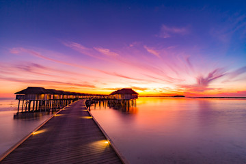 Sunset in Maldives island. Beautiful sunset sky and clouds, luxury water villas and wooden pathway...