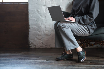 cropped shot of girl in grey clothes and stylish shoes using laptop