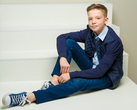 A school-age boy is sitting on a white staircase.