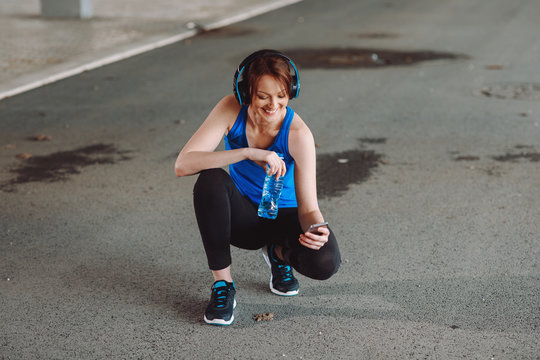 Young woman resting and drinking water after jogging