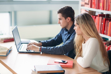 University students sitting together at table with books and laptop. Happy young people doing group study in library