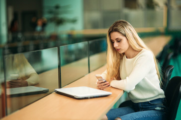 Blonde girl use phone in library