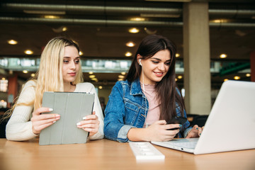 Two girl student use tablet and laptop in library