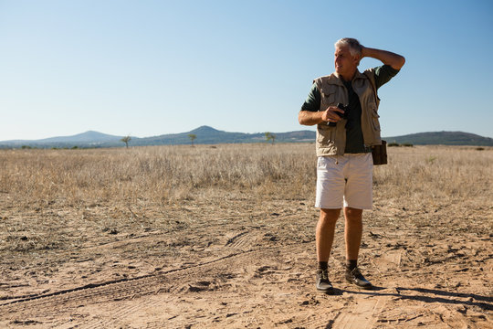 Man with binocular looking away while standing on landscape