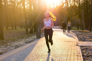 Obraz premium Young girl in headphones enjoys jogging in park at sunset