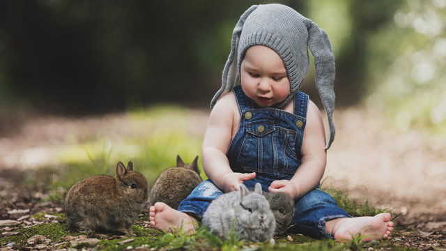 Baby boy sitting with rabbits on grass