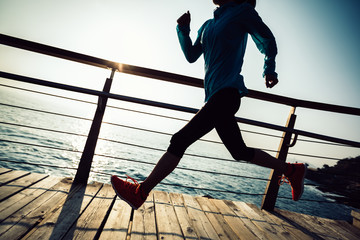sporty fitness female runner running on seaside boardwalk during sunrise
