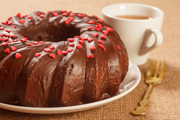 Homemade chocolate cake decorated with small hearts made of caramel on plate, cup of tea and fork on table