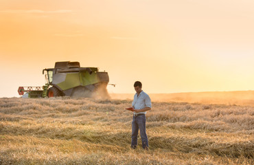 Engineer with notebook and combine harvester in field