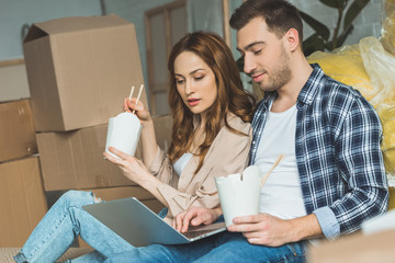 couple eating asian food while using laptop at new apartment, moving home concept
