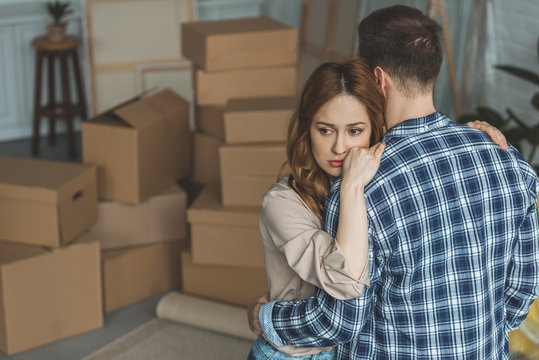 couple hugging at new apartment full of cardboard boxes, moving home concept