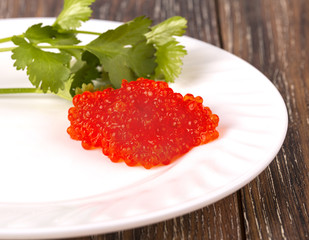 red caviar on a white plate with herbs on wooden