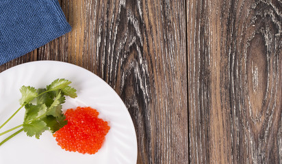red caviar on a white plate with herbs on wooden table