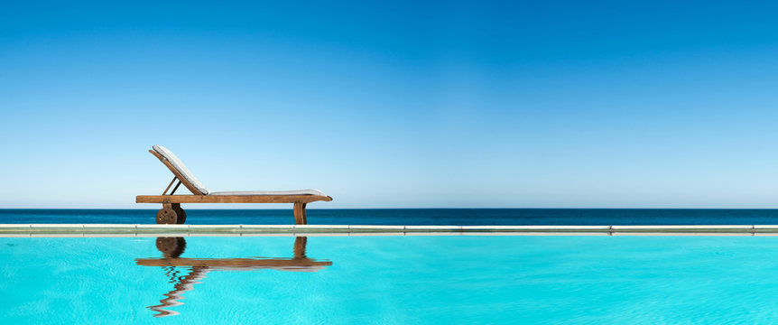 Reclining chair near a swimming pool, sea and blue sky panoramic background