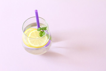 Glass of water, lemon and mint. Glass of pure water and fresh organic lemon and mint isolated on purple background. Detox and healthy food concept