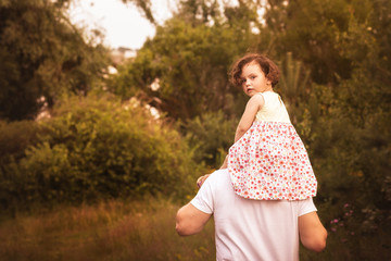 little girl is sitting on her father's shoulders in the summer in the park
