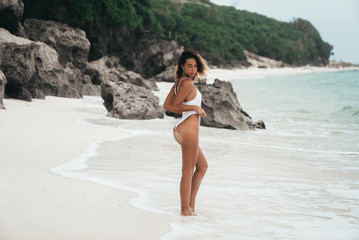 Charming girl with a beautiful ass is walking on the beach. Rear view of a young woman resting near the ocean in a white bikini. Sports body, beauty girl portrait