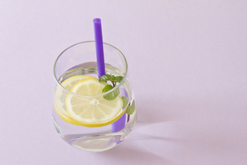 Glass of water, lemon and mint. Glass of pure water and fresh organic lemon and mint isolated on purple background. Detox and healthy food concept.