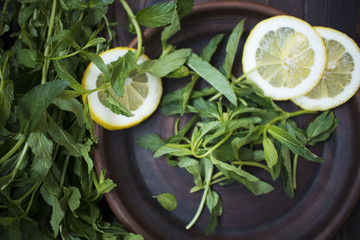 mint leaves and lemon slices on clay plate on wooden background