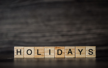 word holidays, consisting of light wooden square panels on a dark wooden background