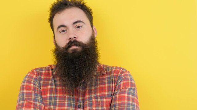 Hipster with long beard on yellow background looks at the camera then touches his beard. At the end of the clip he is smiling to the camera. Available in 4K resolution