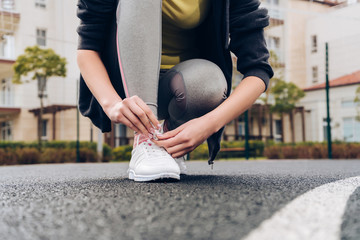 Naklejka premium active young girl trains on a sports ground in open air, ties up shoelaces on sneakers