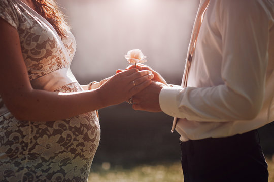 Couple expecting a child holding hands with rose flower facing each other.