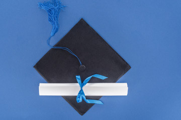 Graduation hat and diploma with blue ribbon isolated on blue