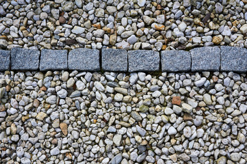 Old gray paving stones in a row surrounded by pebbles