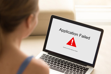Girl looking at laptop with Application Failed error on screen. Software failure, app stopped working, computer unit broke, system crashed unexpectedly, malware concept. Close up, focus on screen.