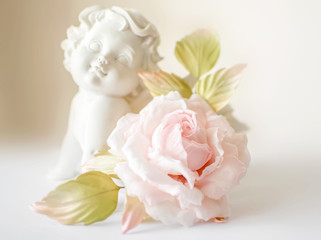 Beautiful flower in light pink cream and white colors rose hand made on white blurred background with angel or amur statuette. Vintage retro style card or decoration. Fashionable female corsage brooch