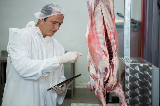 Male butcher maintaining records on digital tablet