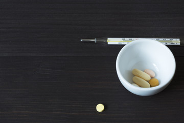 Medications and thermometer on wooden background