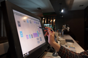 Hand of the waiter holds a fountain pen near the working touch screen monitor.