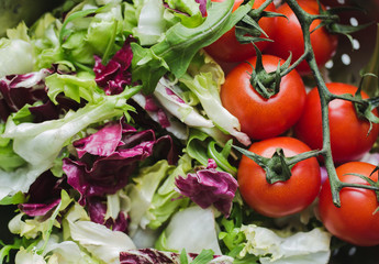 Fresh salad in the steel aluminium colander. Lettuce, arugula and red cherry tomatoes on the vine. Vegan summer food in the kitchen on old vintage wooden background. Vegetarian and healthy vegetables.