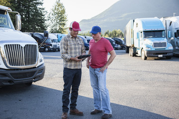 Truck driver team of Caucasian drivers going over dispatch information in the parking lot of a truck stop.