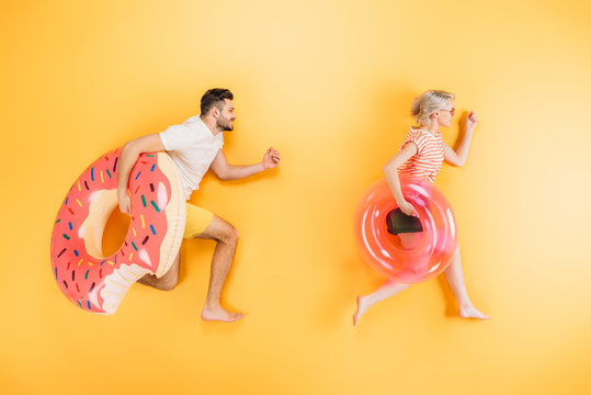 happy young couple holding inflatable swimming rings on yellow