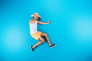 Fototapeta na wymiar top view of young man in shorts and hat posing on blue